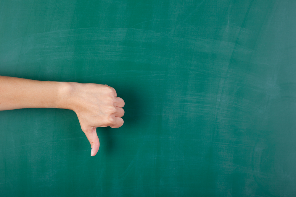 Closeup of woman's hand gesturing thumbs down against chalkboard